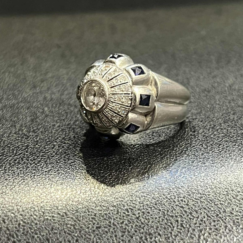 Bague en or blanc 18K sertie d’un diamant central entouré de petits diamants et de saphirs