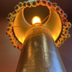 Lamp in de vorm van een "stenen fles" met een blauwe en veelkleurige lampenkap, handgeweven in India.